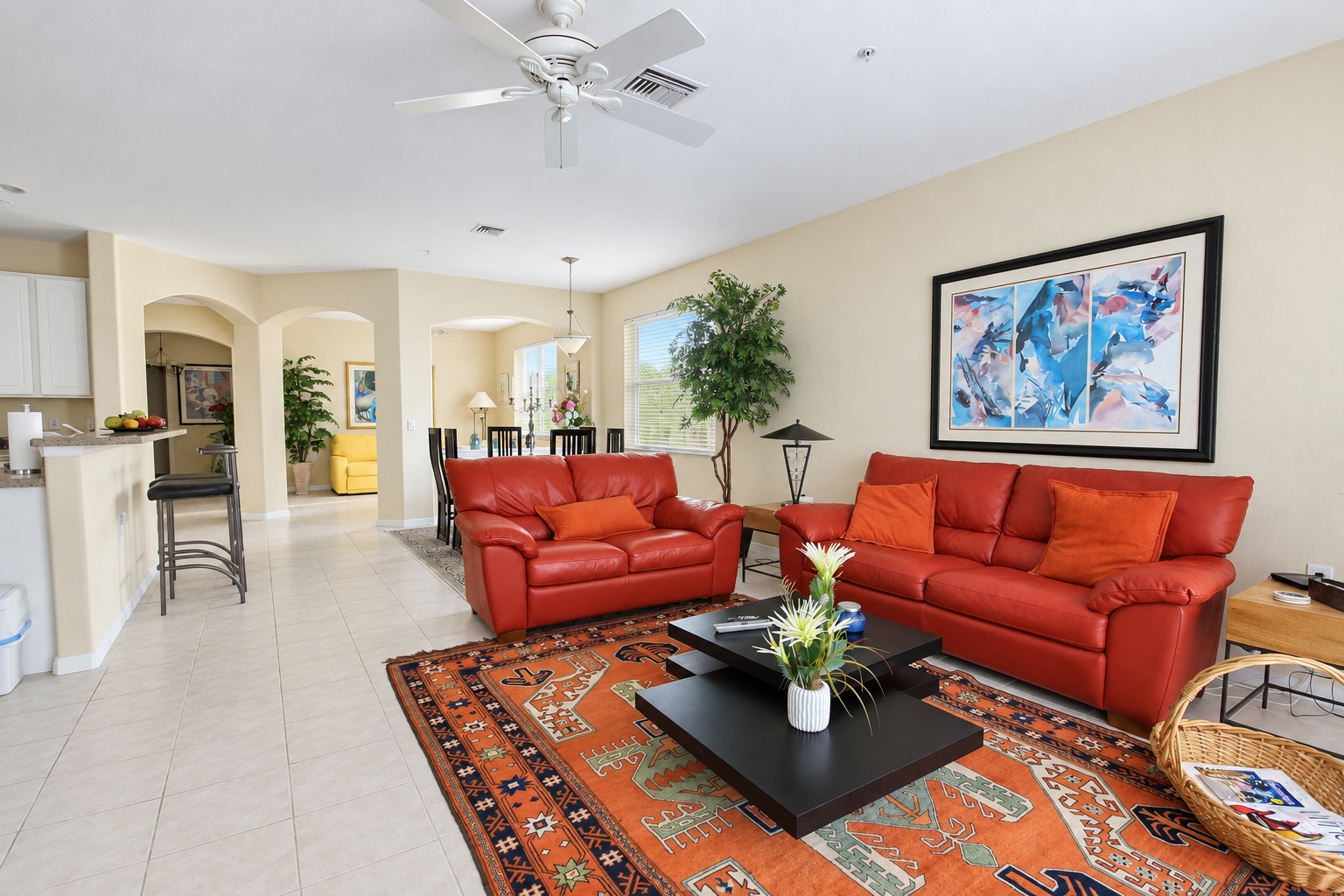 Bright open living room with red leather sofas, ceiling fan and dining area