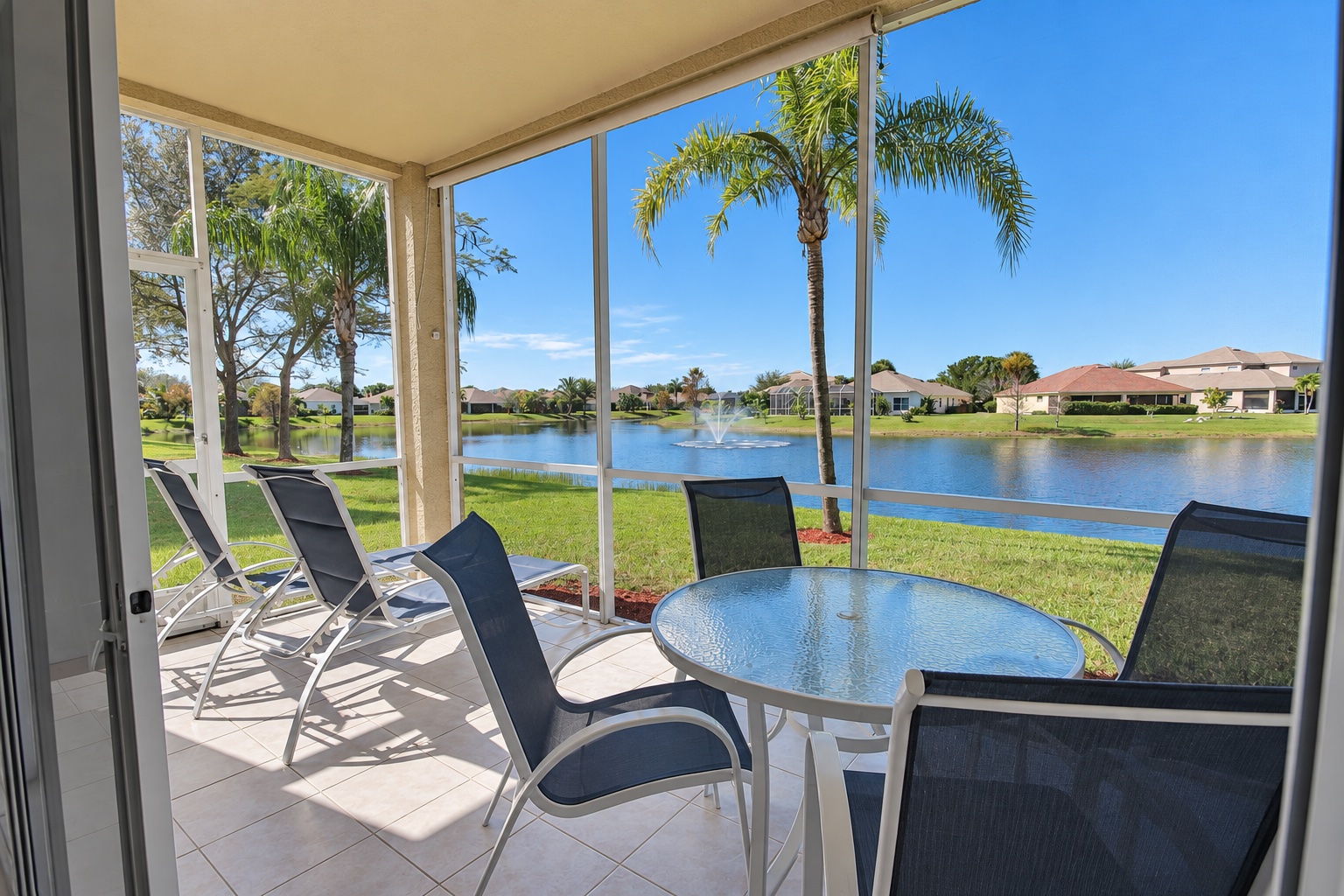Covered lanai with seating and loungers overlooking palms, lake and fountain